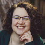 Dr. Wolff's Face in circular image, smiling at camera, she is white, with brown curly hair wearing glasses