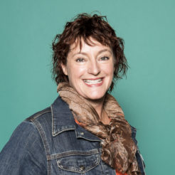 Headshot of smiling woman, auburn hair, jean jacket and scarf, green background