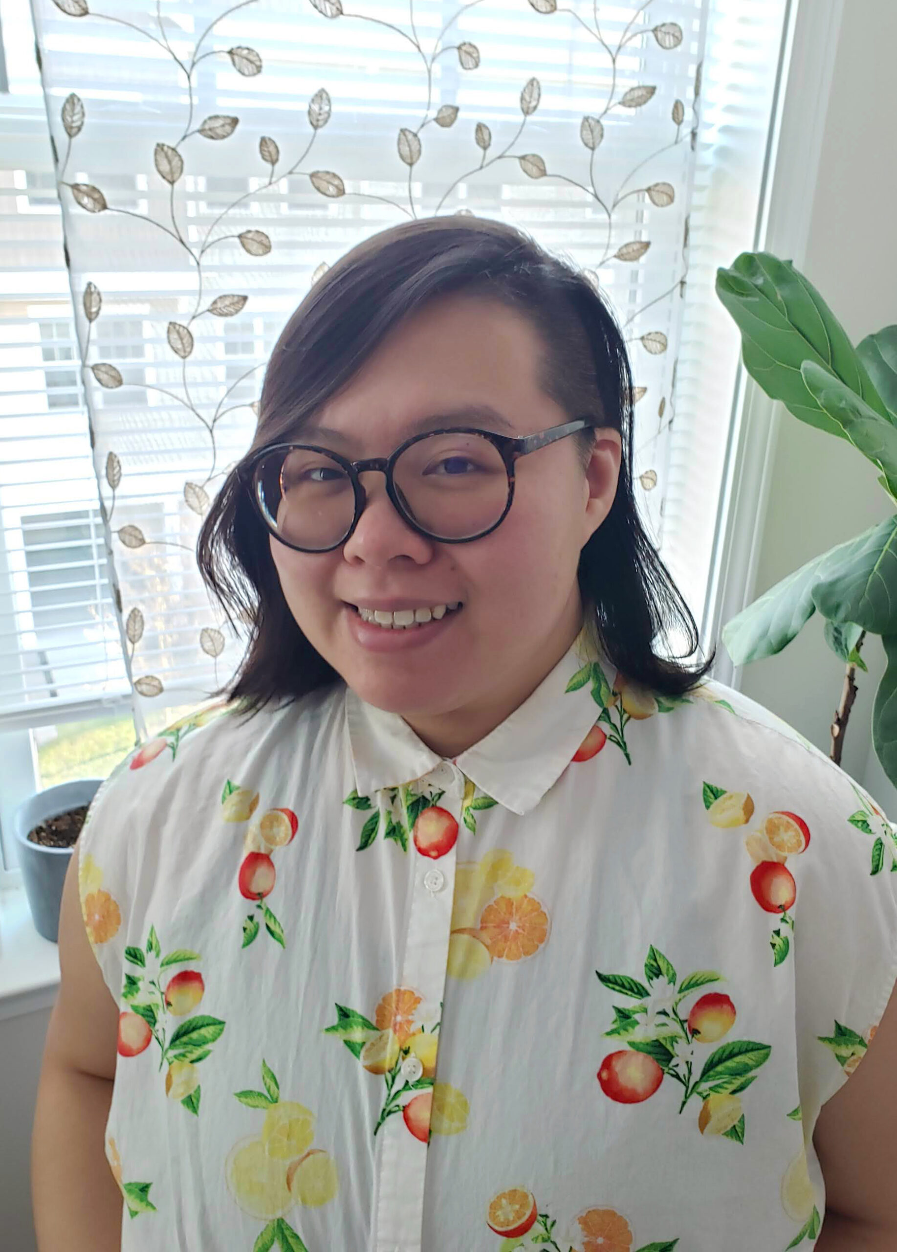 photo of ren lee, a chinese american therapist with light skin, dark hair, with glasses. they are wearing a button up and are in front of a bright window and green plants